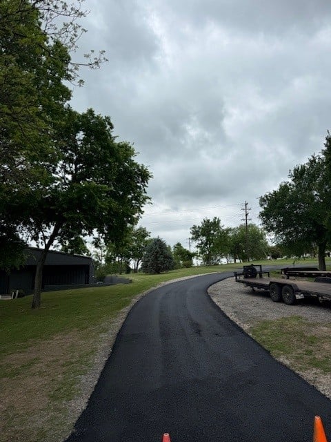 Curved asphalt driveway lined with mature trees and orange traffic cones under cloudy sky