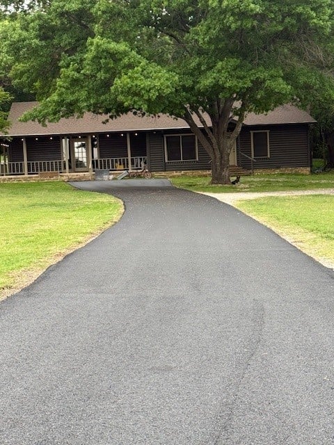 Single-story dark house with white railings and large tree in front, curved asphalt driveway on green lawn